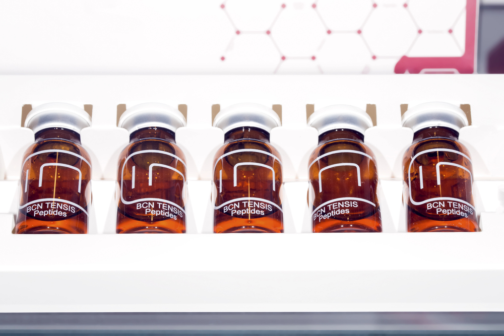 Five amber vials of BCN Tensis Peptides serum in white display tray, peptide skincare product lineup